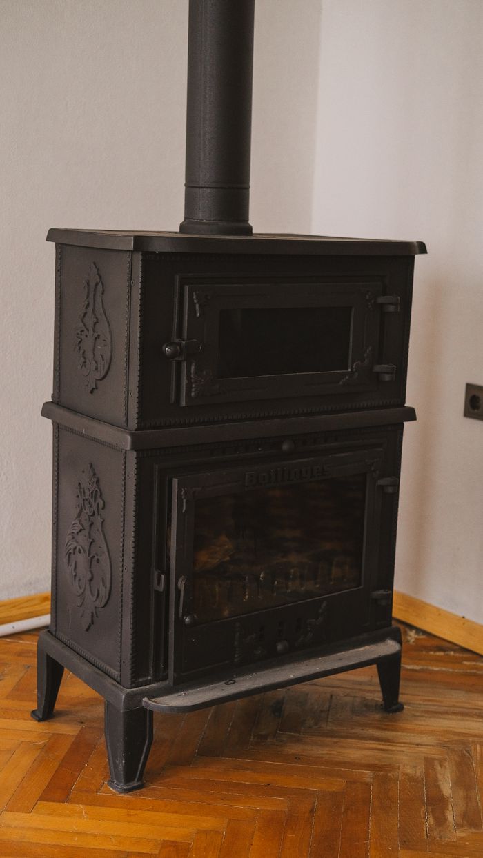 A vintage black iron wood stove in a cozy room with parquet flooring, exuding warmth and rustic charm.